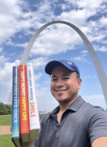 Jason Vitug in Gateway Arch National Park in St. Louis holding best financial wellness books.
